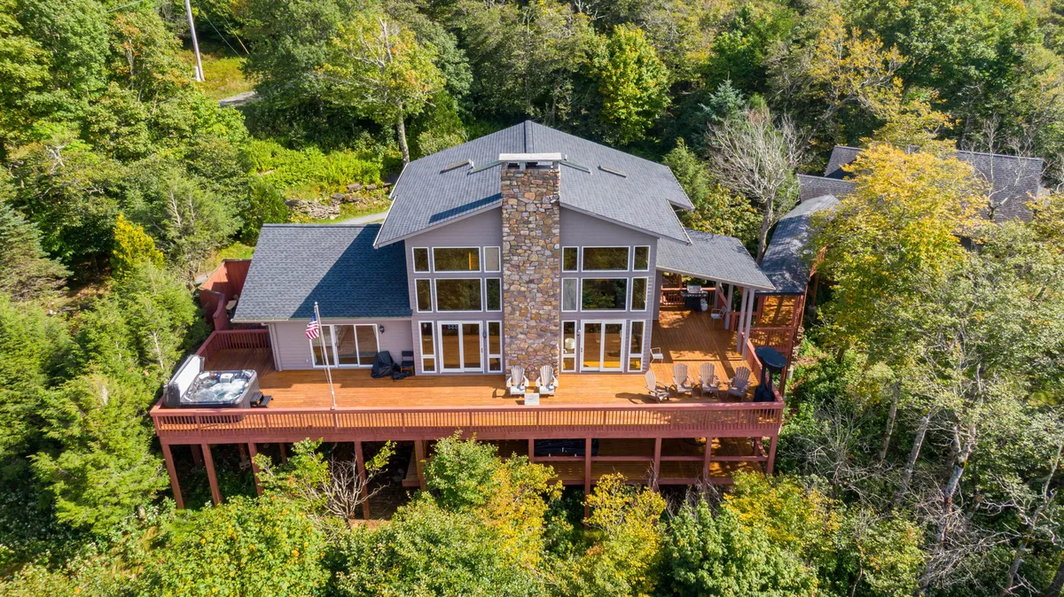 This exterior view shows the chalet's large windows and stone chimney, with a spacious outdoor seating area surrounded by greenery. The tranquil setting is ideal for relaxing, sipping morning coffee, or enjoying the fresh mountain air. The space feels both intimate and connected to the natural surroundings.