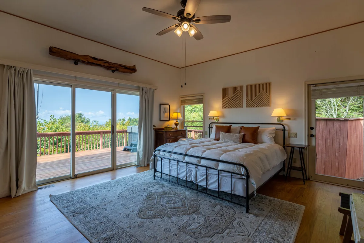 A tranquil bedroom with a comfortable bed, sliding glass doors, decorative wall panels, and a nightstand with a lamp. Natural light pours in, creating a restful escape that embodies comfort and privacy.