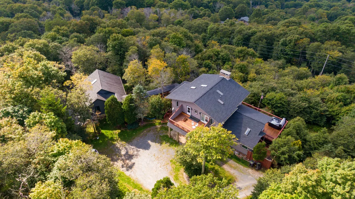 This exterior shot features the main house with a welcoming deck area, surrounded by trees, as well as an adjacent building. The scene highlights the proximity and layout of the two homes, with communal outdoor spaces and nature acting as both a connector and a buffer.