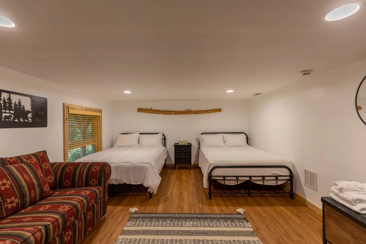A warm, comfortable bonus room featuring two beds, a colorful couch, decorative wall art, and a cozy rug. The arrangement is inviting for group stays, offering flexibility and additional sleeping space.