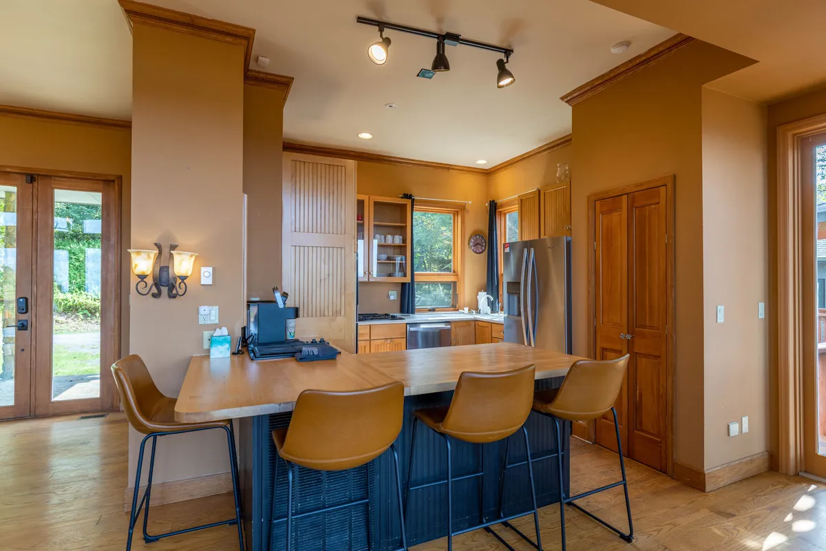 A modern, inviting kitchen with a spacious island and bar stools, light wood cabinetry, and generous windows. The setup encourages socializing during meal preparation, with an open connection to the broader living and dining areas implied.