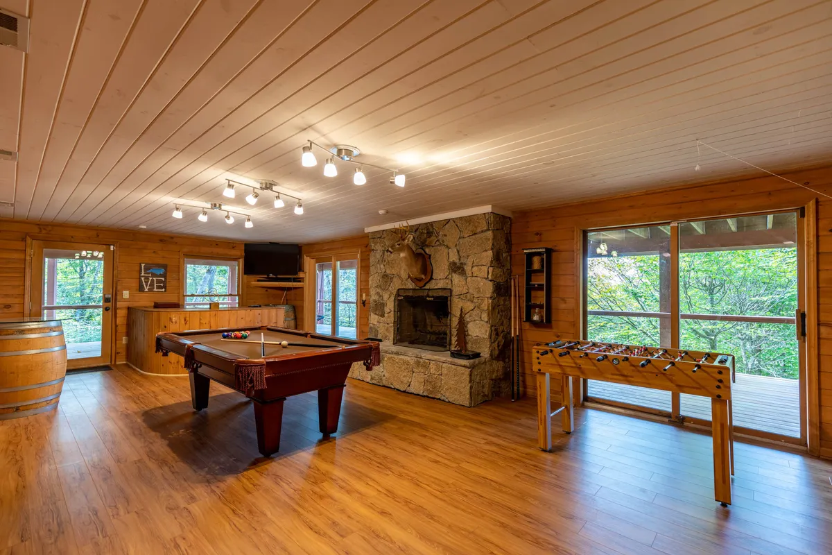 A stylish game room outfitted with a pool table, foosball table, a cozy fireplace, and large windows that let in natural light. The inviting space is designed for recreation and socializing, ideal for après-ski or family game nights.