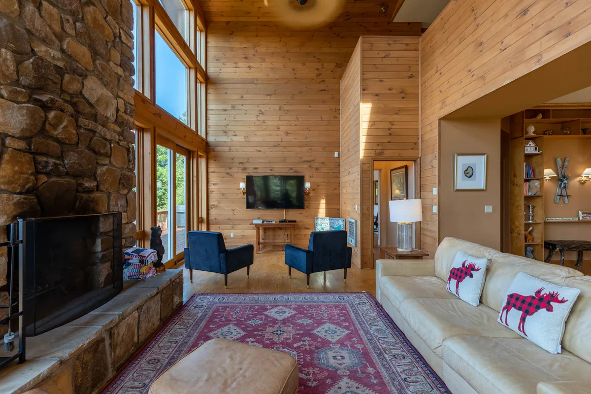 An inviting great room with a stone fireplace, large windows framing scenic views, comfortable seating, and a decorative rug—perfect for gatherings or cozy evenings.