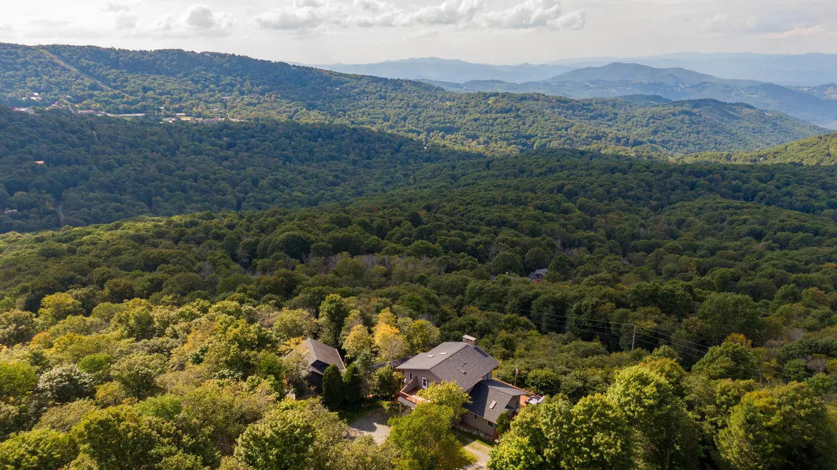 A wide view of the surrounding landscape, with a modern house nestled among trees and expansive skies. The scene conveys a sense of vastness and connection to nature, with clear opportunities for hiking, birdwatching, and exploring right outside the door.