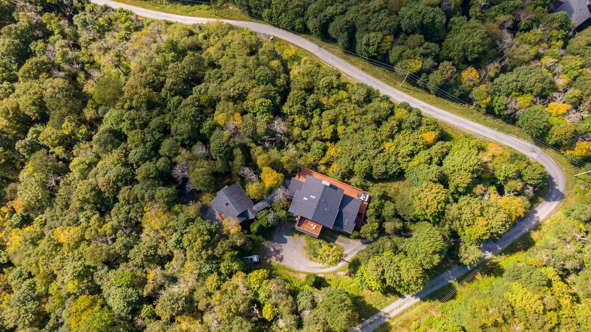 An exterior shot of the main house surrounded by mature trees, with a curved road leading up to the property. The natural landscape hints at the seclusion and tranquility of the setting, while the house looks impressive yet inviting, nestled on the mountainside.
