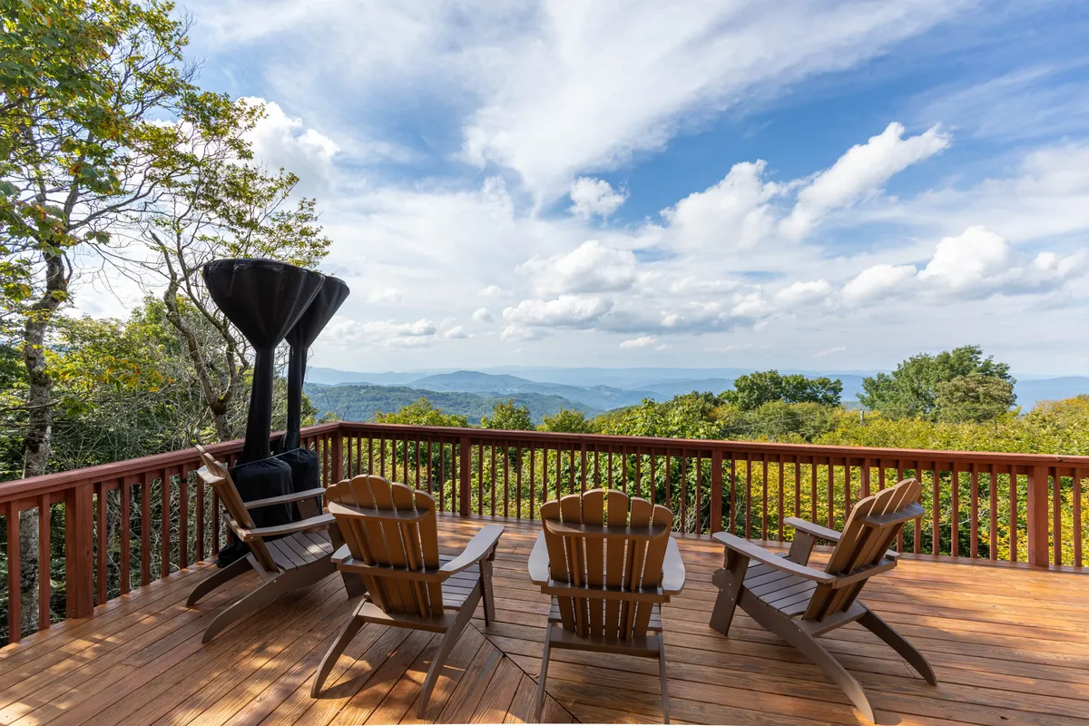 This image features Adirondack chairs set on a deck overlooking expansive mountain views, framed by a sturdy deck railing. The setting suggests a tranquil spot for unwinding while taking in the natural surroundings, with open skies that hint at both daytime and evening possibilities.