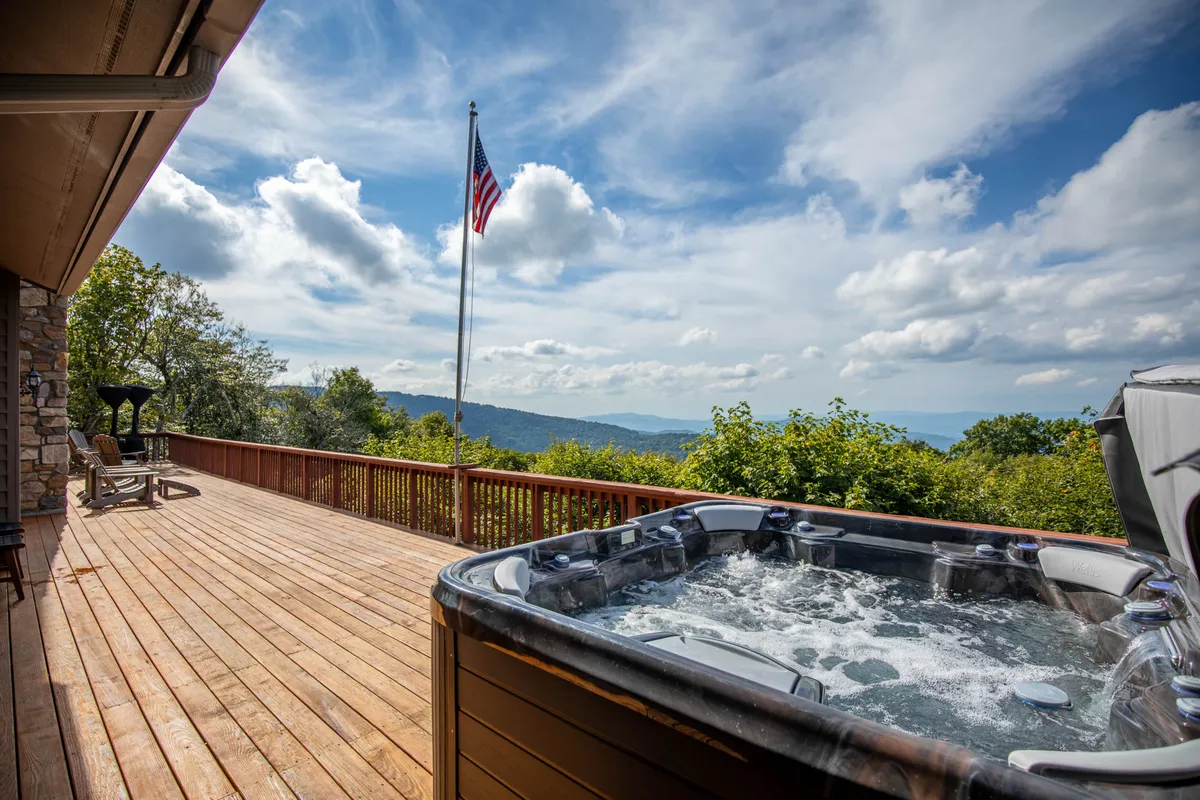 This image features a hot tub on a wooden deck with an American flag and a panoramic mountain view. The scene conveys a tranquil atmosphere with the promise of relaxation and scenic vistas, perfect for a morning coffee or an evening soak.