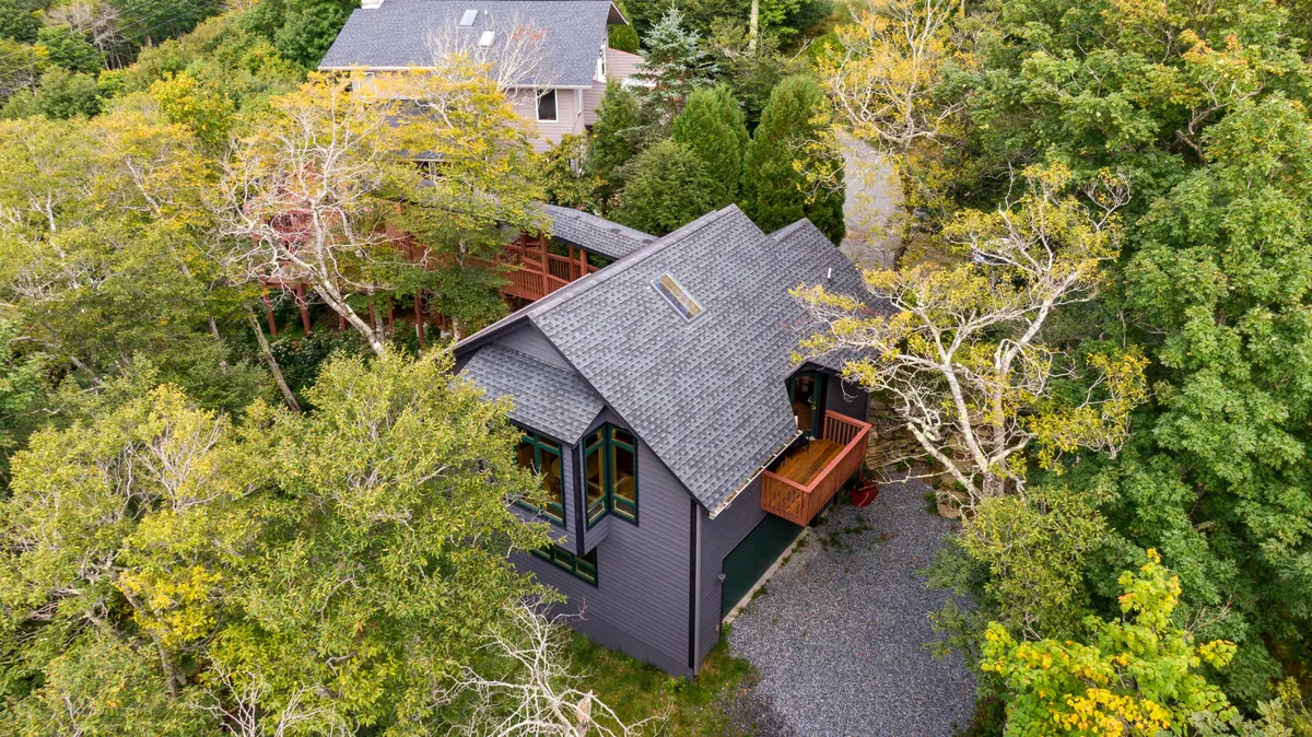 A serene exterior shot of the property featuring the house surrounded by mature trees and a gravel pathway winding toward the entrance. The setting is calm and secluded, perfect for leisurely walks or just soaking in the mountain atmosphere together.