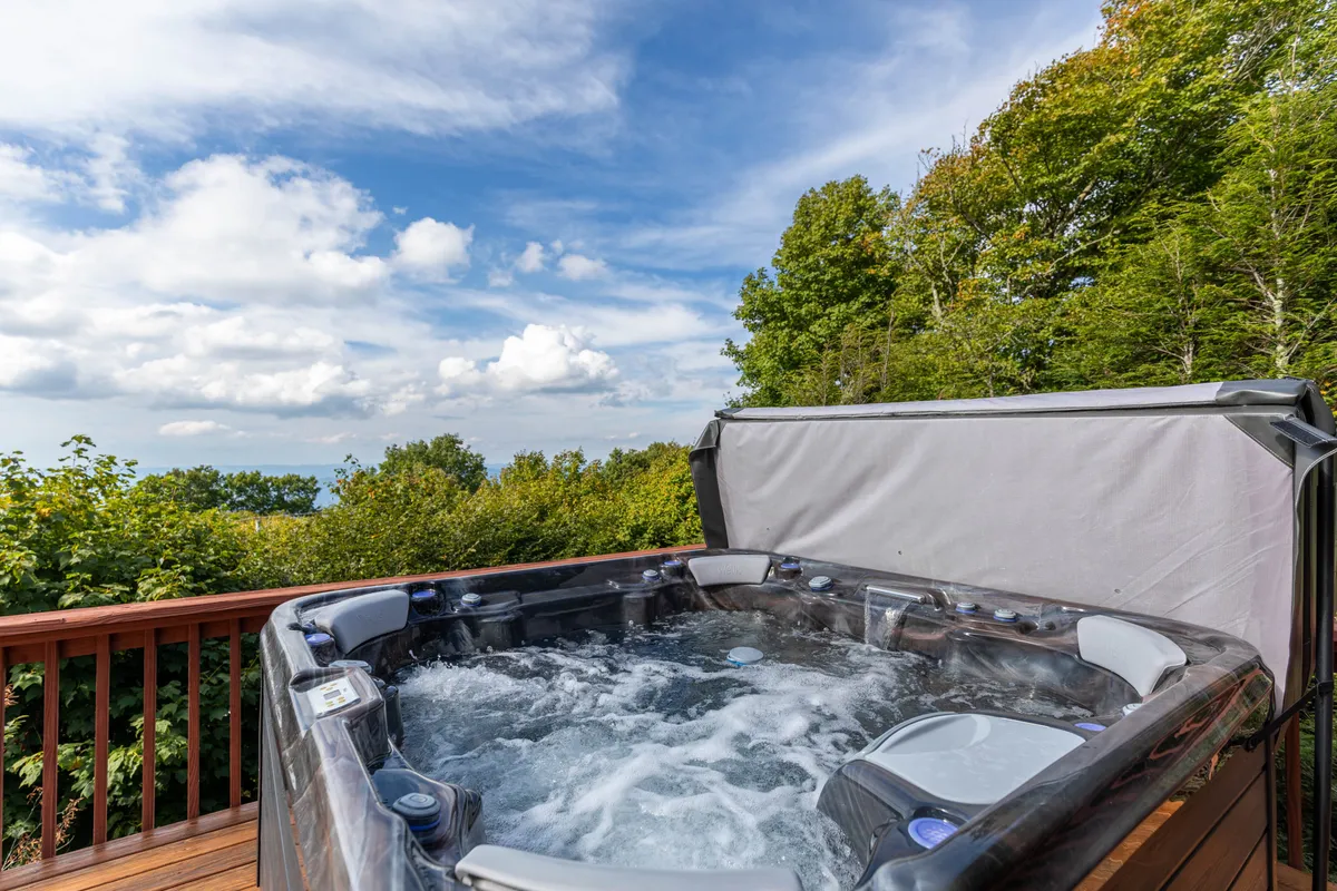 A serene outdoor hot tub set amidst lush greenery with an open sky above. The inviting tub offers a space for relaxation, framed by the peaceful mountain environment—perfect for ending a day of adventure in comfort.